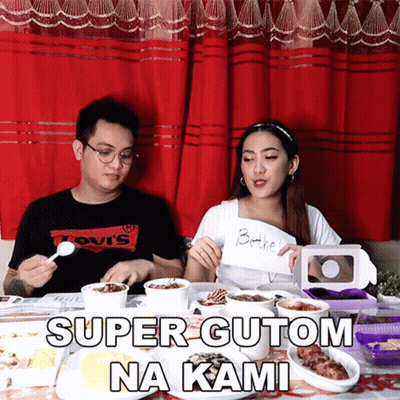 A Man Wearing A Levis Shirt Sits At A Table With A Woman Holding A Sign That Says Super Gutom Na Kami GIF
