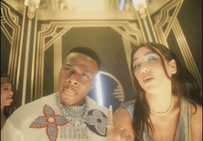 A Man Wearing A Louis Vuitton Sweater Stands Next To A Woman Wearing A Pearl Necklace GIF