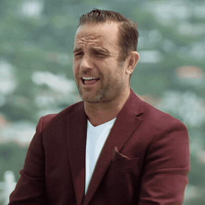 A Man Wearing A Maroon Jacket And A White Shirt Is Making A Funny Face GIF