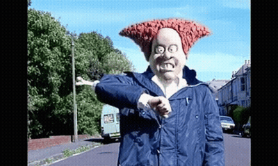 A Man Wearing A Mask And A Blue Jacket Is Giving A Thumbs Up While Standing On A Street . GIF