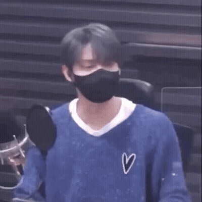 A Man Wearing A Mask And A Blue Shirt Is Sitting In Front Of A Microphone . GIF