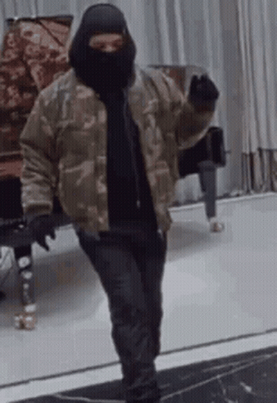 A Man Wearing A Mask And A Camouflage Jacket Is Standing In A Room . GIF