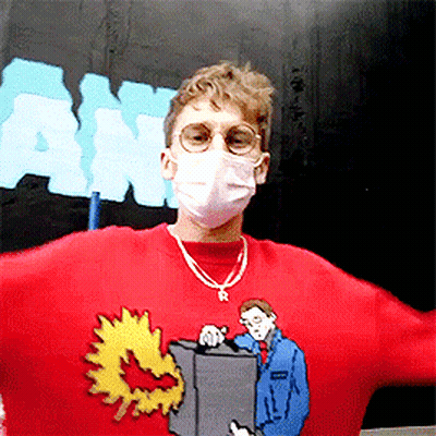 A Man Wearing A Mask And A Red Sweater With A Man Holding A Box GIF