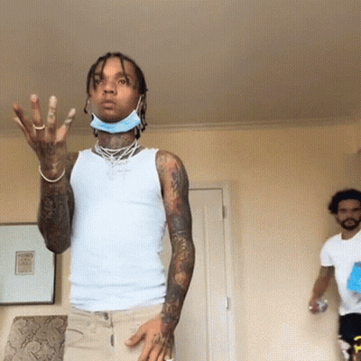 A Man Wearing A Mask And A White Tank Top Is Standing In A Room With Another Man . GIF