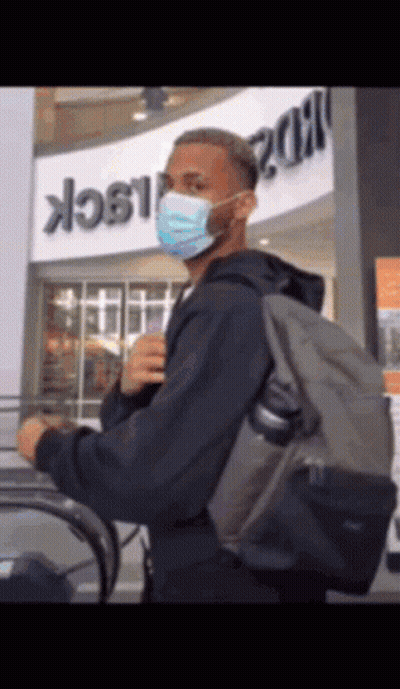 A Man Wearing A Mask And Carrying A Backpack Is Riding An Escalator GIF