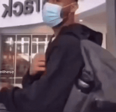 A Man Wearing A Mask And Carrying A Backpack Is Standing In Front Of A Sign That Says Lock GIF