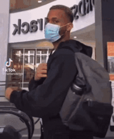 A Man Wearing A Mask And Carrying A Backpack Is Walking On An Escalator . GIF