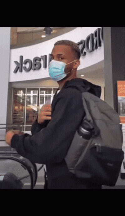 A Man Wearing A Mask And Carrying A Backpack Stands In Front Of A Building That Says Black GIF