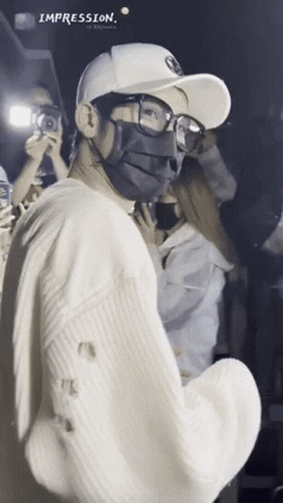 A Man Wearing A Mask And Glasses Is Standing In Front Of A Crowd With The Word Impression Above Him GIF