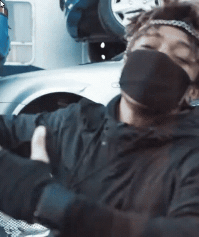 A Man Wearing A Mask And Gloves Is Sitting In Front Of A Car . GIF