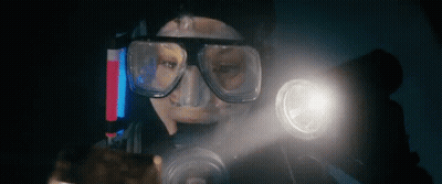 A Man Wearing A Mask And Goggles Is Holding A Flashlight In His Hand . GIF