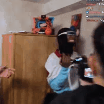 A Man Wearing A Mask And Goggles Is Standing In A Room Holding A Remote Control . GIF