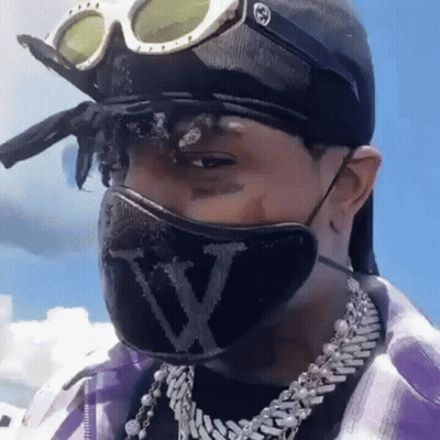 A Man Wearing A Mask And Goggles Is Wearing A Hat And A Necklace . GIF
