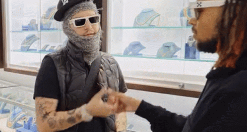 A Man Wearing A Mask And Sunglasses Talks To Another Man In A Jewelry Store GIF