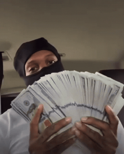 A Man Wearing A Mask Holds A Stack Of 100 Dollar Bills In Front Of His Face GIF