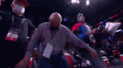 A Man Wearing A Mask Is Being Escorted Out Of A Stadium . GIF