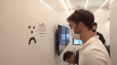 A Man Wearing A Mask Is Looking At A White Board With A Smiley Face Drawn On It GIF