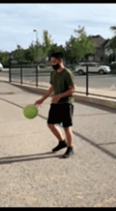 A Man Wearing A Mask Is Playing With A Ball On The Sidewalk GIF