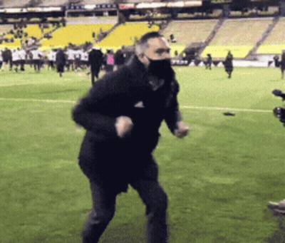 A Man Wearing A Mask Is Running On A Soccer Field . GIF