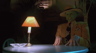 A Man Wearing A Mask Is Sitting At A Table With A Lamp On GIF