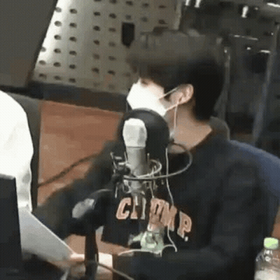 A Man Wearing A Mask Is Sitting In Front Of A Microphone In A Radio Station . GIF