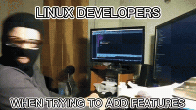 A Man Wearing A Mask Is Sitting In Front Of Two Computer Monitors With The Words Linux Developers When Trying To Add Fea GIF