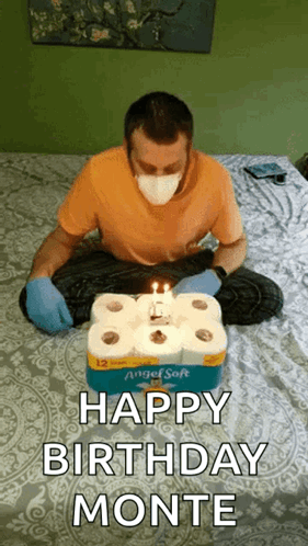 A Man Wearing A Mask Is Sitting On A Bed With A Birthday Cake Made Out Of Toilet Paper . GIF