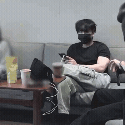 A Man Wearing A Mask Is Sitting On A Couch Looking At His Cell Phone GIF