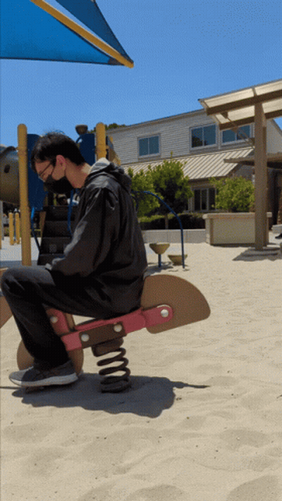 A Man Wearing A Mask Is Sitting On A Rocking Horse In The Sand GIF