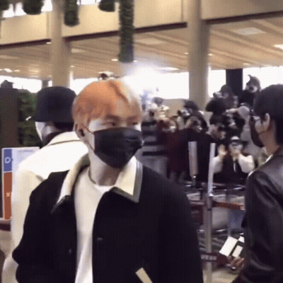 A Man Wearing A Mask Is Standing In Front Of A Crowd Of People At An Airport . GIF