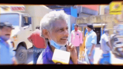 A Man Wearing A Mask Is Talking Into A Microphone While Standing In A Crowd . GIF