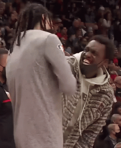 A Man Wearing A Mask Laughs With Another Man In A Crowd GIF