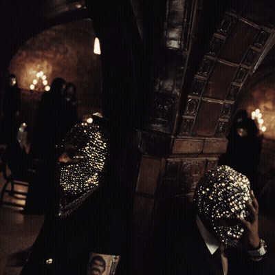 A Man Wearing A Mask With Rhinestones Is Standing In A Dark Room GIF