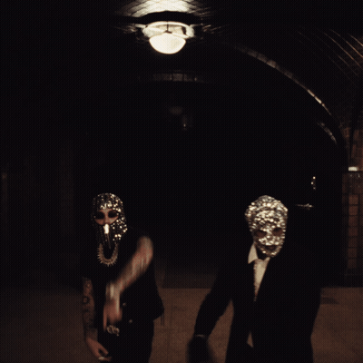 A Man Wearing A Mask With Rhinestones On It Stands Next To Another Man In A Suit GIF