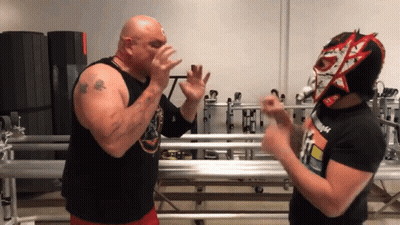 A Man Wearing A Mask With The Letter N On It Stands Next To A Bald Man GIF