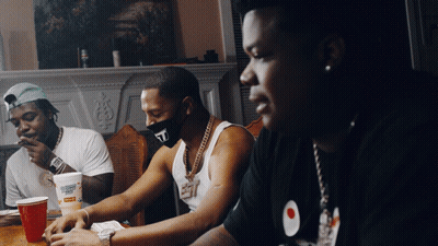 A Man Wearing A Mask With The Letter T On It Sits At A Table With Other Men GIF