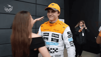 A Man Wearing A Mclaren Racing Suit Talks To A Woman GIF