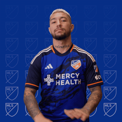 A Man Wearing A Mercy Health Jersey Stands In Front Of A Blue Background GIF