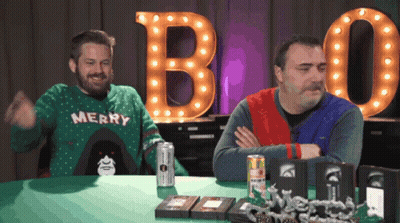 A Man Wearing A Merry Sweater Is Sitting At A Table GIF