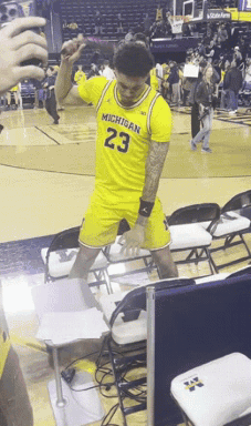 A Man Wearing A Michigan Jersey Is Dancing On The Court GIF