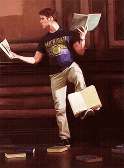 A Man Wearing A Michigan Shirt Is Holding A Book In His Hand GIF