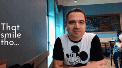 A Man Wearing A Mickey Mouse Shirt Is Smiling In Front Of A Chalkboard That Says That Smile Tho GIF