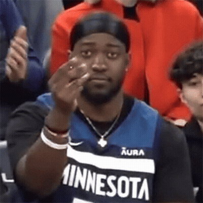 A Man Wearing A Minnesota Jersey Is Giving The Middle Finger While Sitting In The Stands . GIF