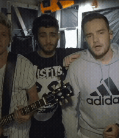 A Man Wearing A Misfits Shirt Holds A Guitar While Standing Next To Two Other Men GIF
