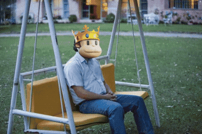 A Man Wearing A Monkey Mask And A Crown Is Sitting On A Swing GIF
