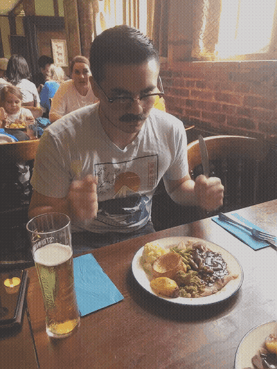 A Man Wearing A Mustache Is Sitting At A Table With A Plate Of Food GIF
