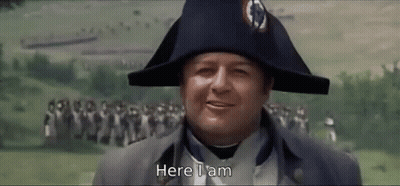 A Man Wearing A Napoleon Hat Is Standing In Front Of A Crowd And Says Here I Am . GIF