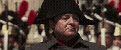 A Man Wearing A Napoleon Hat Stands In Front Of A Crowd Of People GIF