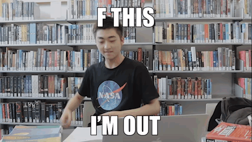 A Man Wearing A Nasa Shirt Is Sitting At A Desk In A Library GIF