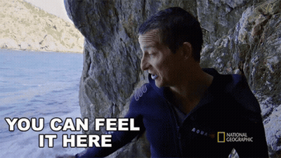 A Man Wearing A National Geographic Jacket Is Standing In Front Of A Body Of Water GIF